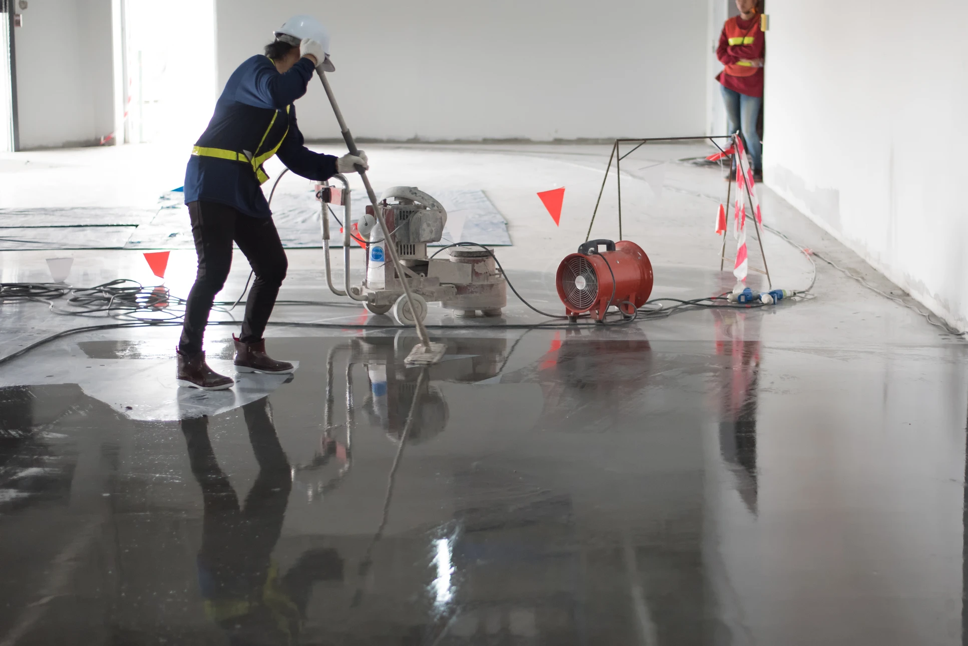 Chantier extérieur avec ouvrier en combinaison de protection effectuant des travaux de sablage sur structures en béton préfabriqué